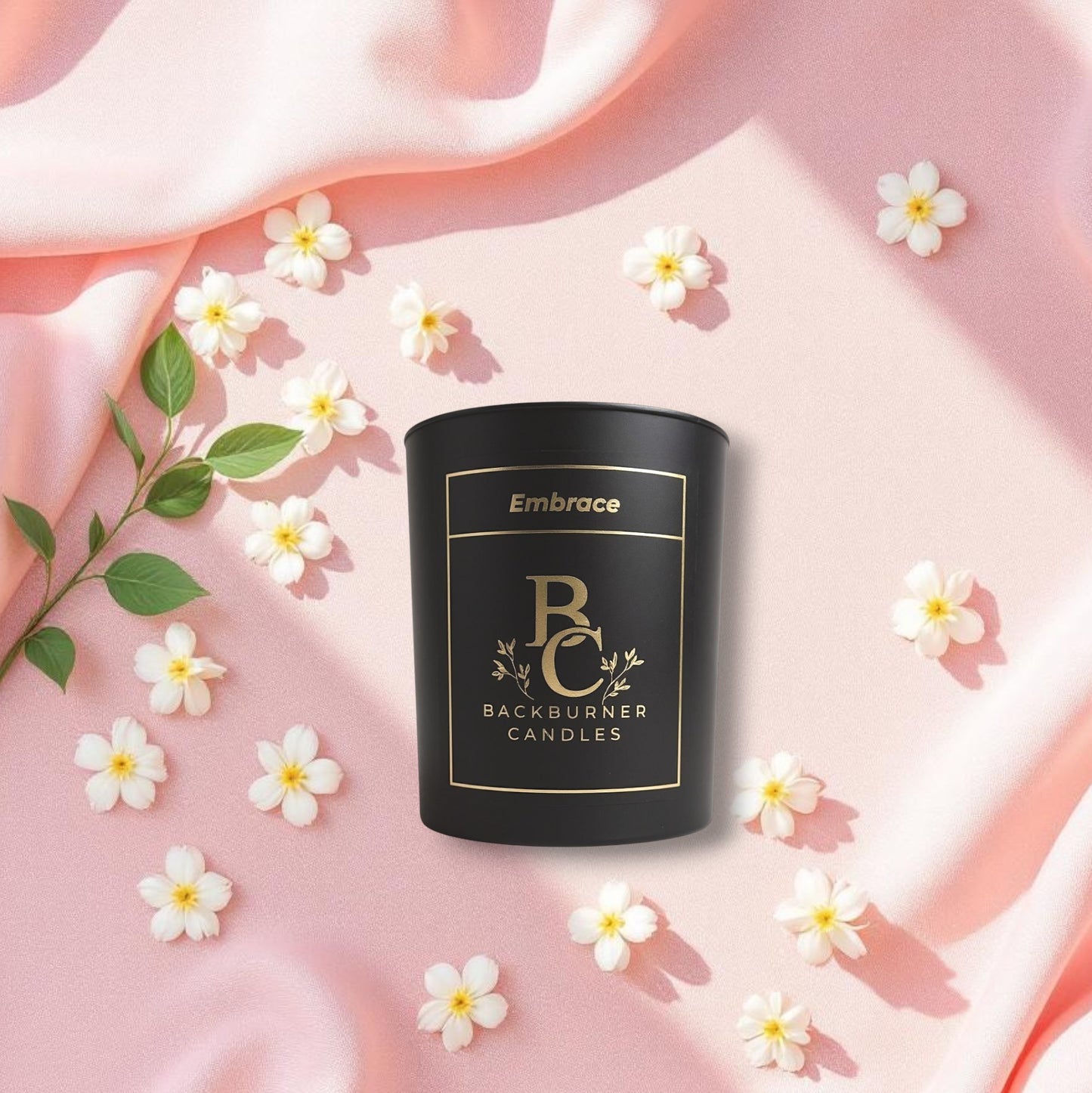 Embrace candle with 'Backburner Candles' branding on a pink fabric background with jasmine flowers
