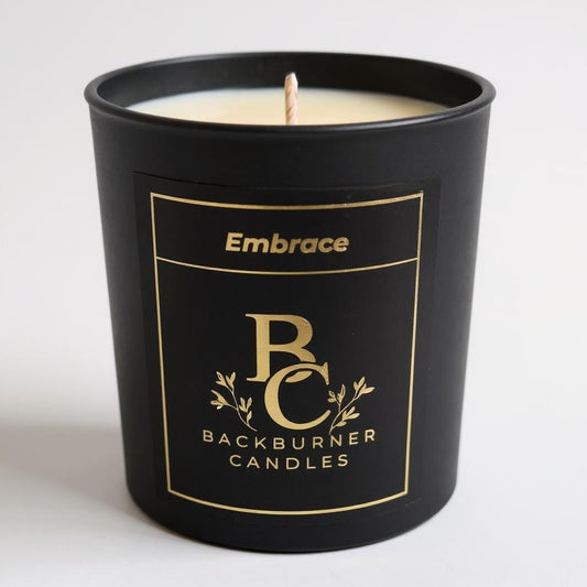 Unlit Embrace vegan candle by Backburner Candles in black jar with gold logo and floral design, styled for a premium, elegant look.