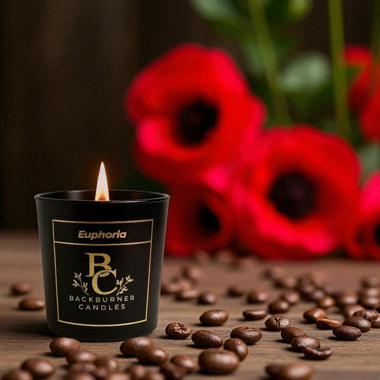 Euphoria candle in black glass jar by Backburner Candles in front of red flowers and coffee beans.