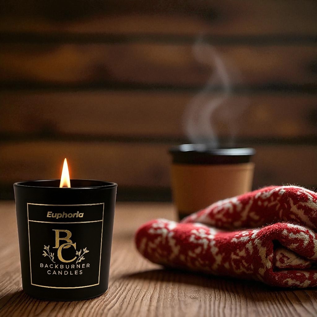 Euphoria candle in black glass jar by Backburner Candles on a wooden surface with a hot drink and a blurred background.