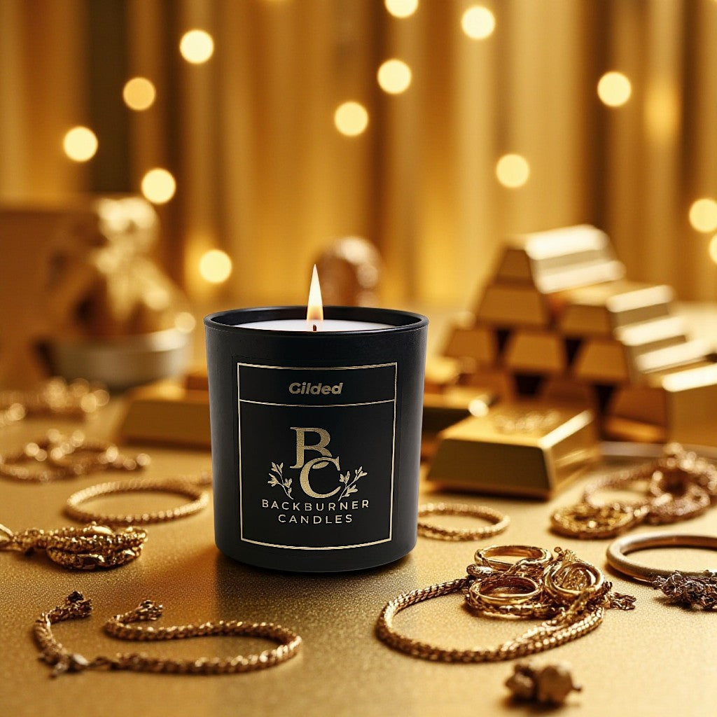 Gilded candle in black glass jar by Backburner Candles on a gold surface with jewellry