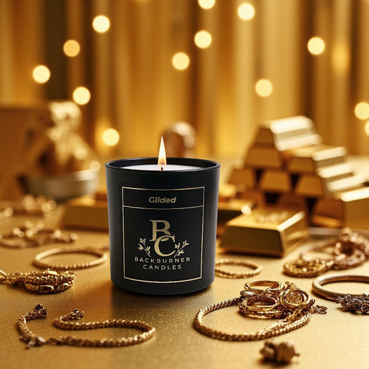 Gilded candle in black glass jar by Backburner Candles on a gold surface with jewellry