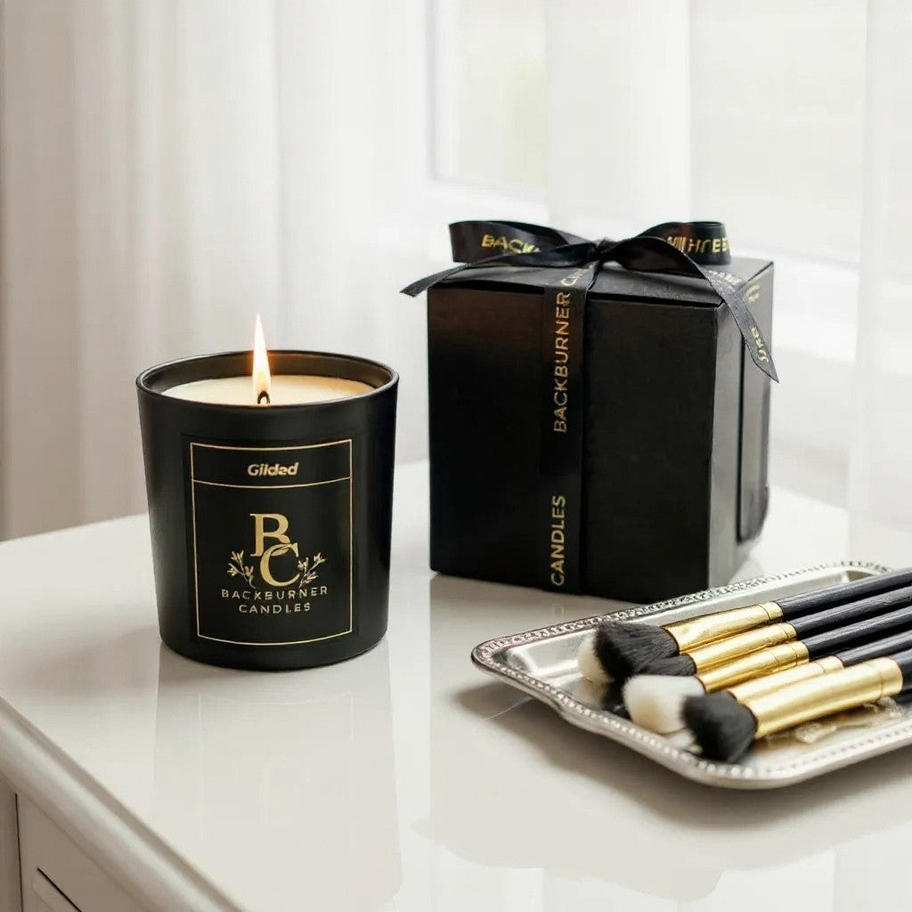Backburner Candles Gilded candle with packaging and makeup brushes on a white surface