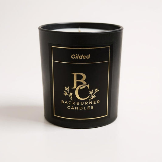 Unlit Gilded vegan candle by Backburner Candles in black jar with gold logo and floral design, styled for a premium, elegant look.