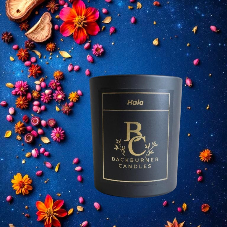 Black candle with 'Backburner Candles' branding on a blue background with flowers and spices.