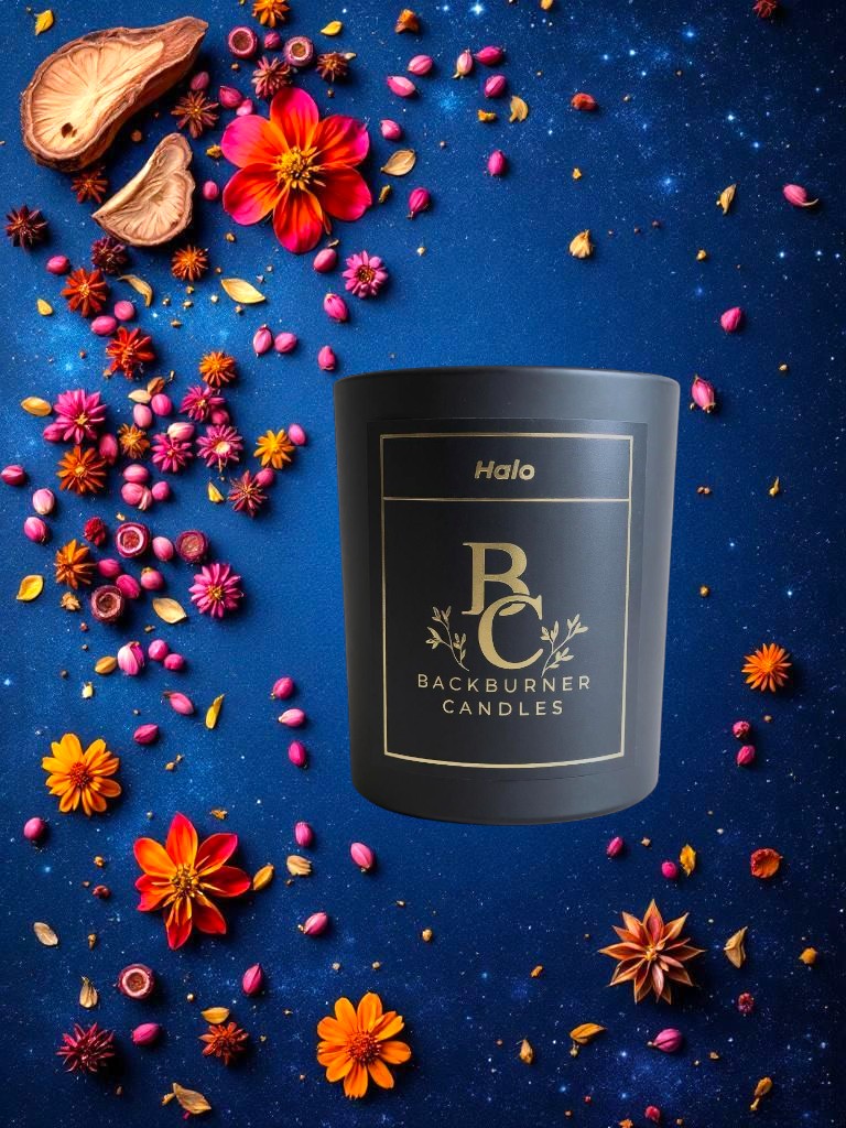 Halo candle in black glass jar by Backburner Candles surrounded by colorful flowers on a blue background