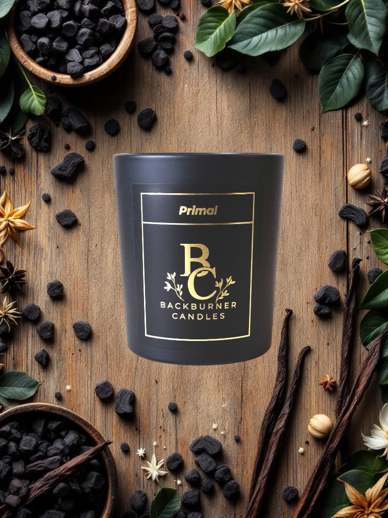 Black Primal candle on a wooden surface with natural elements.
