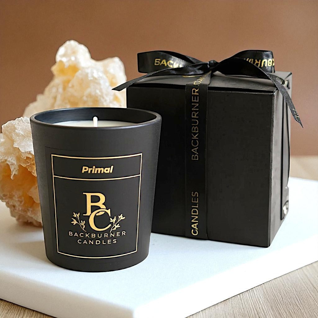 Primal candle by Backburner Candles next to a black gift box on a neutral background