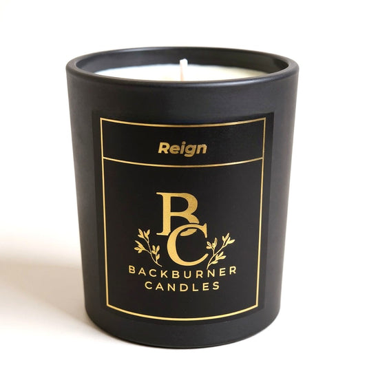 Unlit Reign vegan candle by Backburner Candles in black jar with gold logo and floral design, styled for a premium, elegant look.