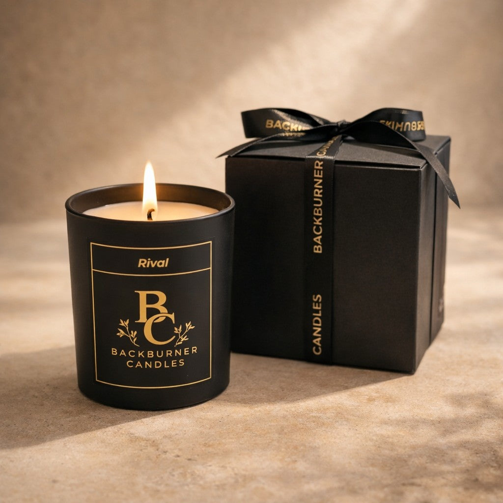 Black candle with 'Backburner Candles' branding next to a black gift box on a beige surface.
