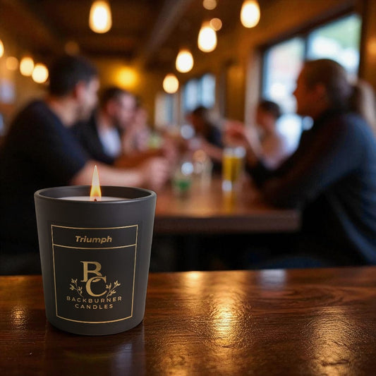 Lit Triumph vegan candle by Backburner Candles on wooden table, styled in cosy bar setting with warm lighting and social ambiance.