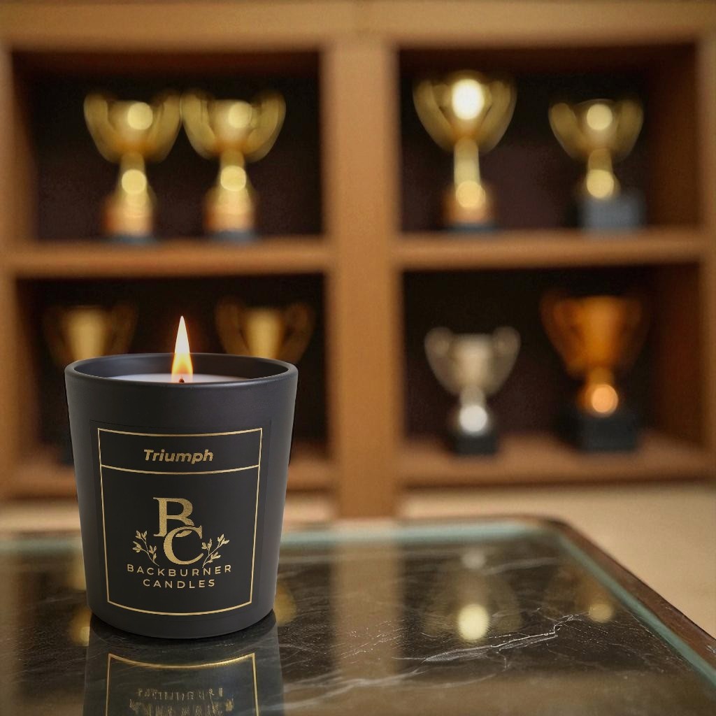 Lit Triumph vegan candle by Backburner Candles on glass surface, styled with trophies for a bold, celebratory and elegant ambiance.