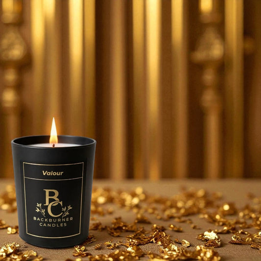 Valour vegan candle by Backburner Candles lit in black jar, styled with gold confetti and a warm, luxurious golden backdrop.