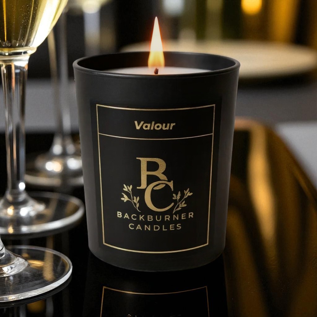 Lit Valour vegan candle by Backburner Candles in black jar with gold design, styled with champagne for a luxurious celebration vibe.