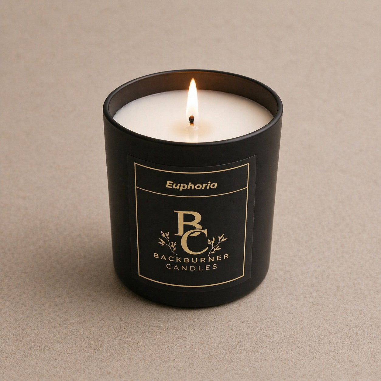 Black candle in a container labeled 'Euphoria' by 'Backburner Candles' on a beige background