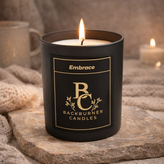 Black candle in a container with 'Backburner Candles' branding on a stone surface.