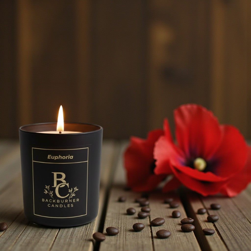Black candle labeled 'Backburner Candles' with a red flower and coffee beans on a wooden surface.