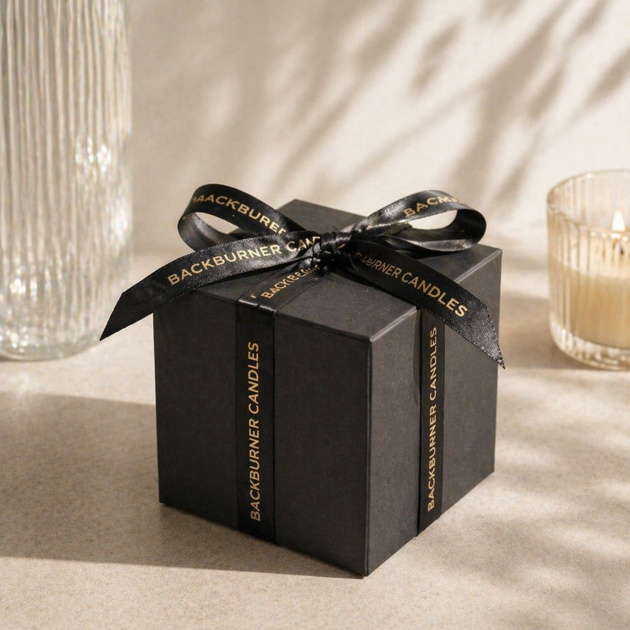 Black gift box with a ribbon featuring 'Backburner Candles' on a neutral background.