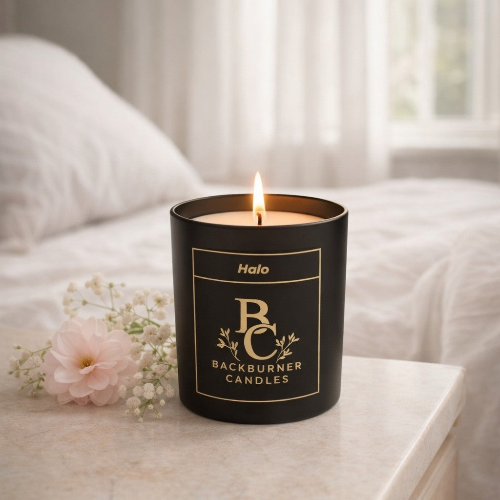 Black candle with 'Backburner Candles' branding on a white surface with a flower.