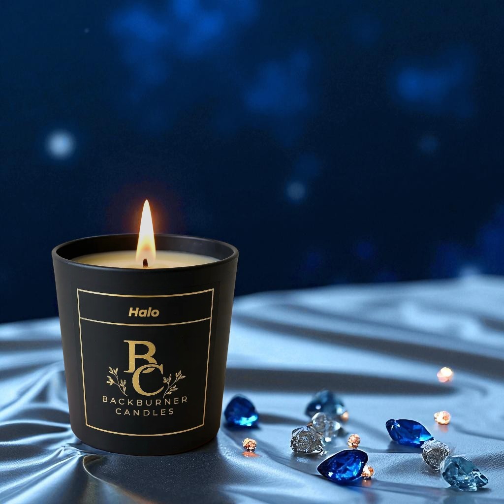 Halo candle in black glass jar by Backburner Candleson a dark fabric background with decorative stones.