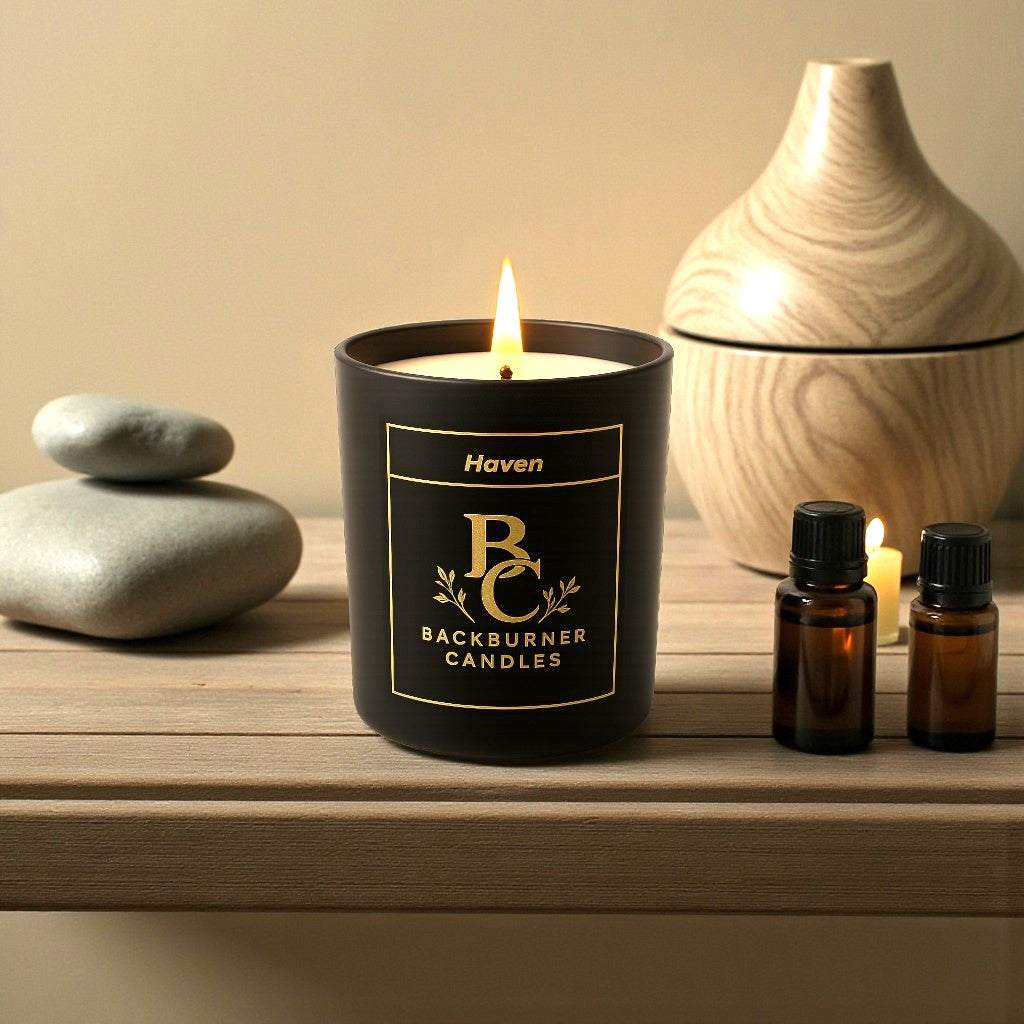 Lit candle with 'Backburner Candles' label on a wooden surface with decorative items.