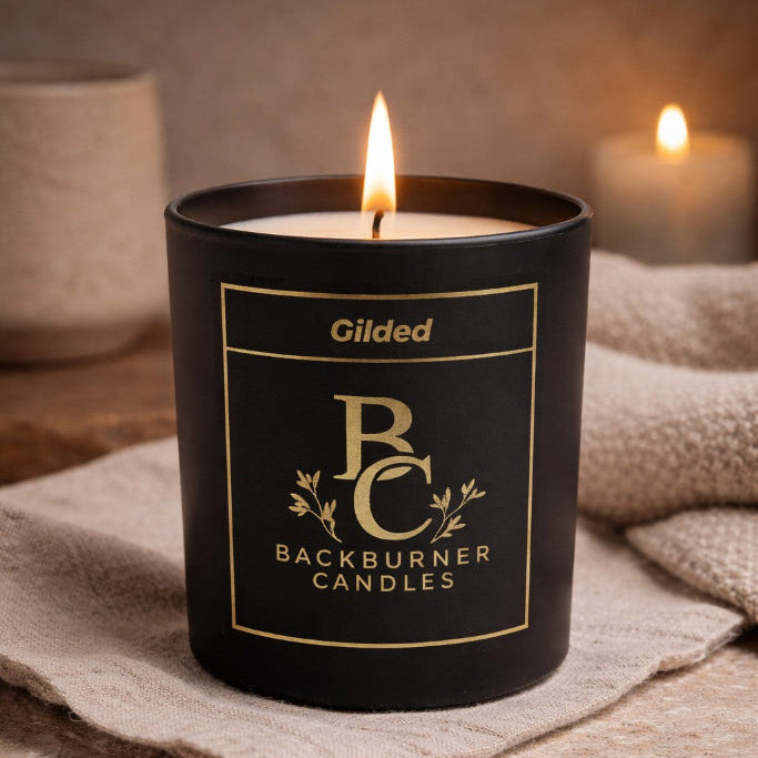 Gilded Backburner Candles candle on a textured surface with a warm glow