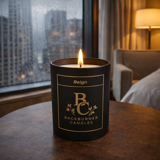 Candle in a black container with 'Backburner Candles' branding on a table by a window.