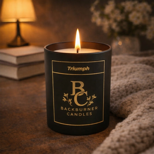 Black candle with 'Triumph Backburner Candles' label on a wooden surface.