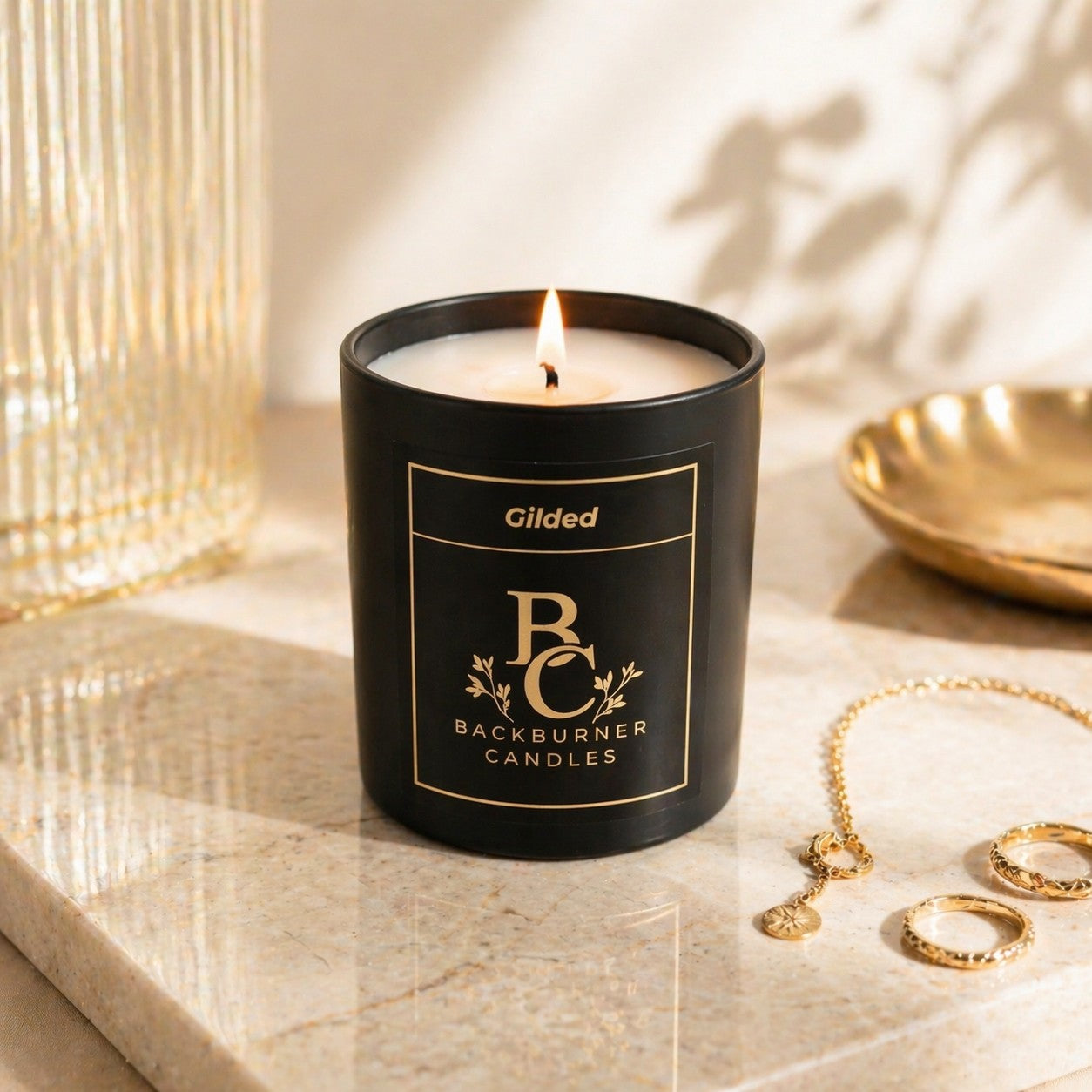 Gilded Backburner Candles candle on a marble surface with jewelry