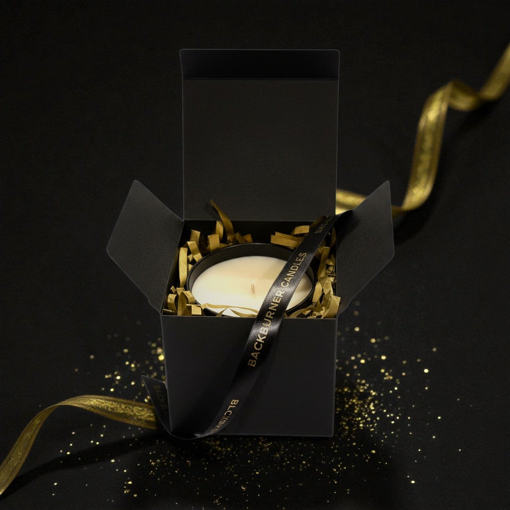 Black gift box with a white candle and gold ribbon on a black background