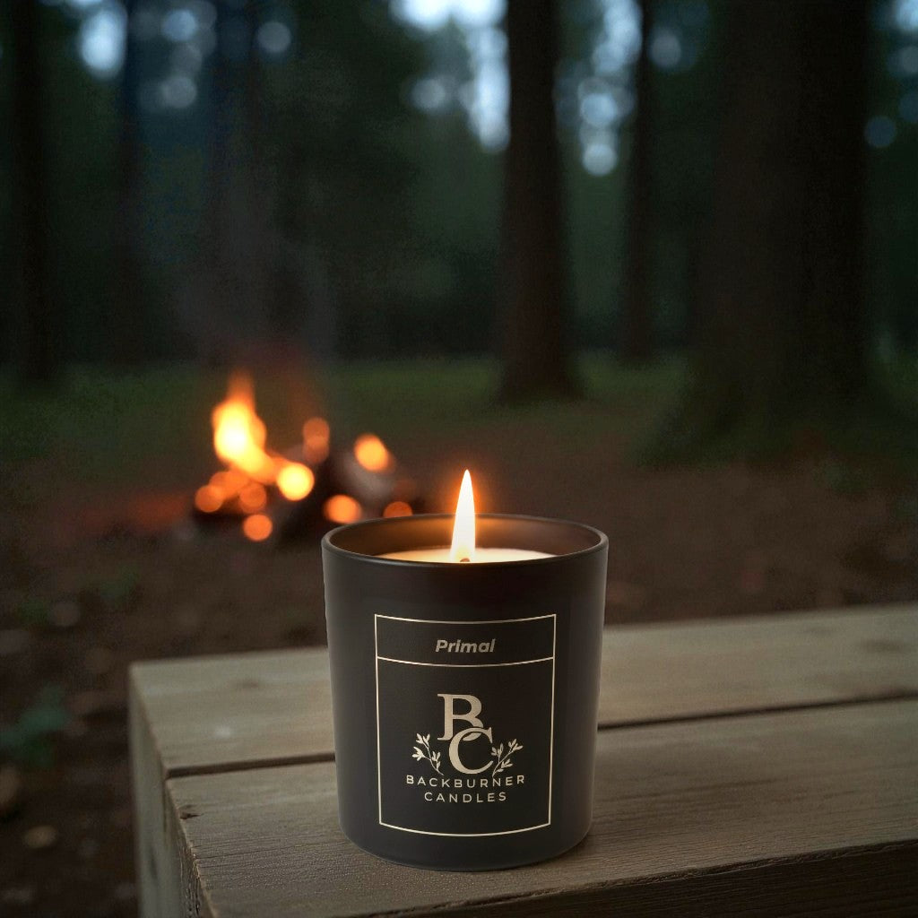 Candle in a black container with 'Backburner Candles' branding in a forest setting.