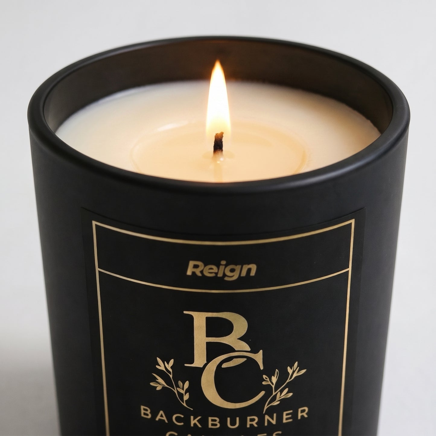 Black candle in a container with 'Reign' branding on a light gray background