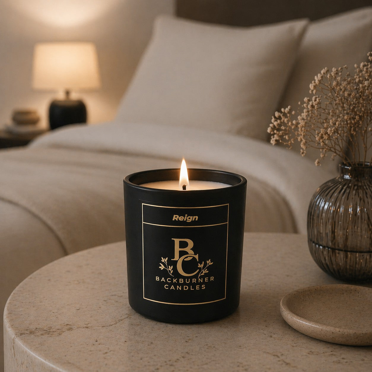 Black candle with 'Backburner Candles' branding on a table in a bedroom setting.
