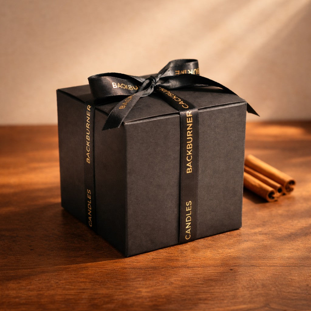 Black gift box with 'Backburner Candles' ribbon on a wooden surface