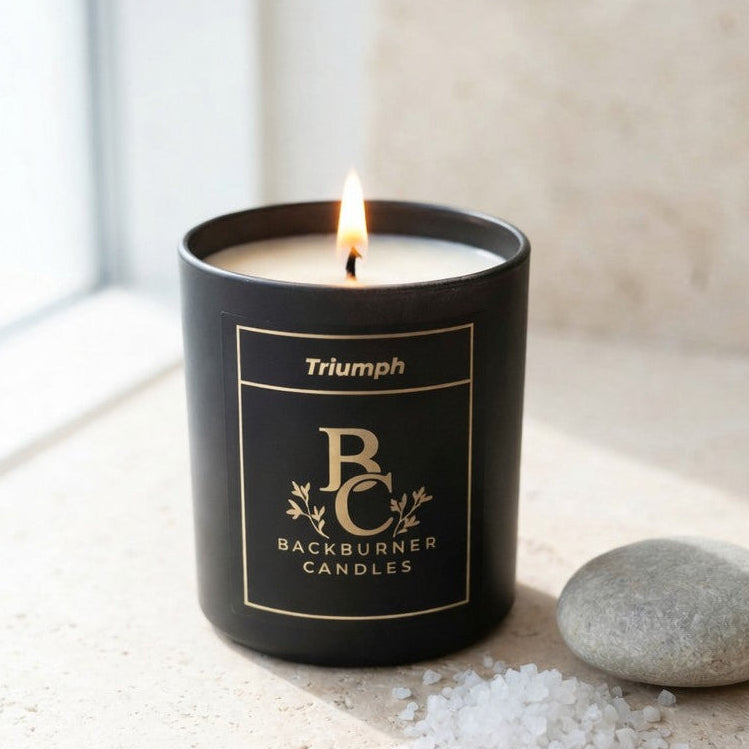 Black candle with 'Backburner Candles' branding on a light surface with a stone and salt crystals.
