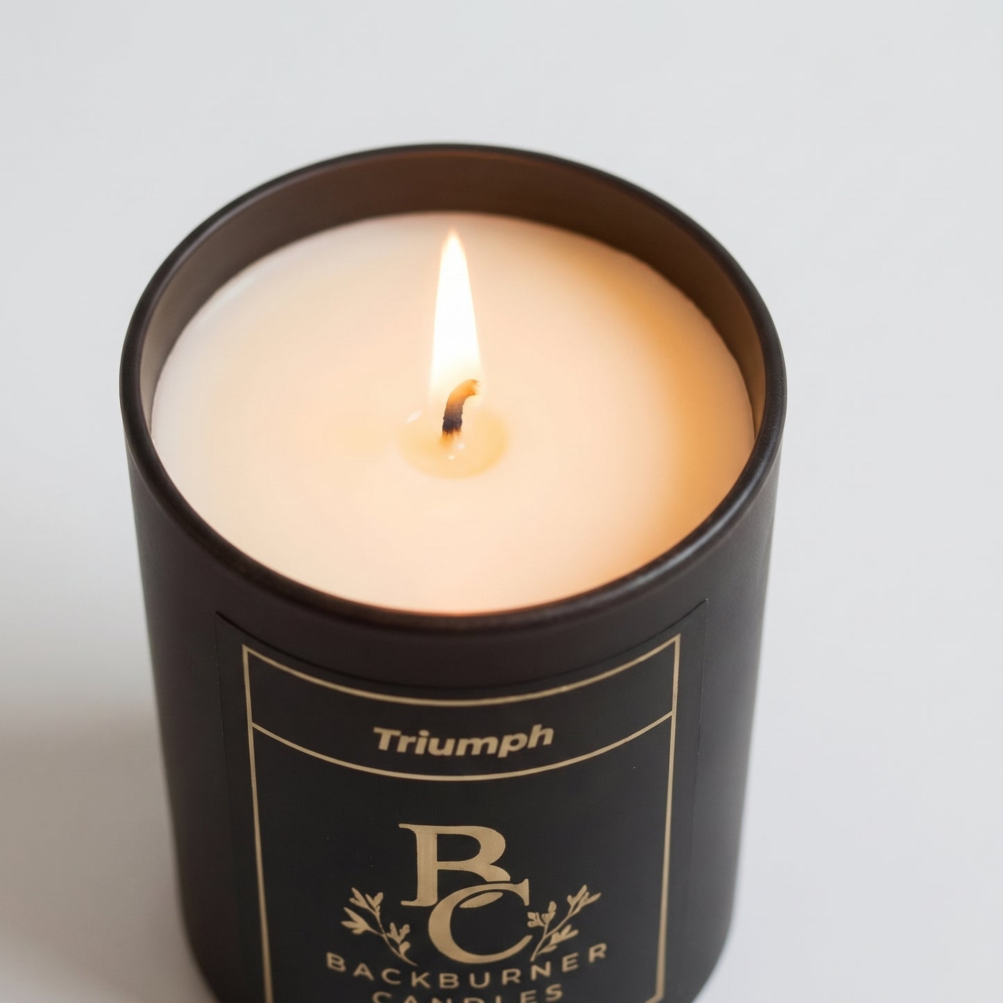 Candle in a black container with 'Triumph' branding on a light gray background